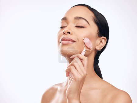 Photo for Cosmetics, woman and facial roller in white studio background for skincare, beauty and slim cheeks. Female person, confident and glowing isolated with tool for removing lines, cleaning and soothing. - Royalty Free Image