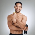 Water, smile and portrait of man with apple in studio for fitness, exercise and healthy diet. Nutrition, workout and shirtless athlete with h2o drink and fruit for hydration by gray background