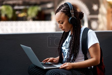 Woman, student and headset with laptop outside, typing and online classes for elearning or education. University, leaner and website research for assignment, listening and podcast or school project.