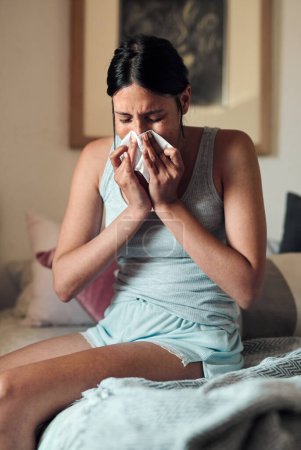 Young, woman and blowing with nose in bedroom for health, virus or infection in spring. Female person, sick and toilet paper in home with cough or allergy, mucus with congestion and headache.