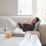 Woman, fatigue and sad or sick in home, cold and medicine for illness and treatment for health. Female person, blanket and virus on couch for burnout, pills and stress for crisis or pain and drugs.