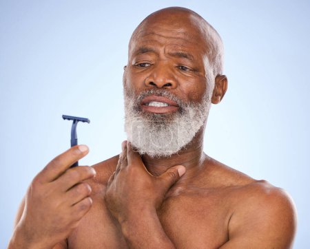 Pain, shaving and black man with razor for beard in studio for grooming, hair removal or self care treatment. Injury, clean and mature person with shaver for facial shaving routine by blue background.