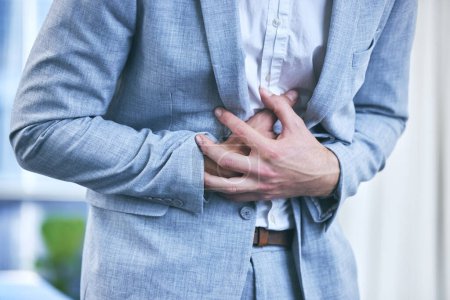 Businessman, office and hands on stomach with pain from diarrhea, food poisoning or ibs in workplace. Indigestion, constipation and bloated from overeating or appendicitis with hernia or poor diet