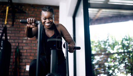 Black woman, cycling and gym for fitness, airbike and gym for sports workout. Exercise, bodybuilder and cardio for body health and wellness, active and challenge for African person in studio.