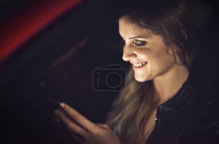 Mujer, sonrisa y smartphone en coche por la noche con transporte para viajar con tecnología para la comunicación. Redes sociales, leer o contestar mensajes de texto con chistes en Nueva York con tnc o taxi