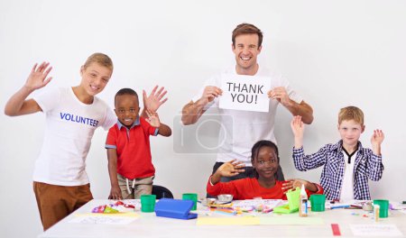 Kindergarten, volunteering and people with children at school for development, fun and learning. Happy, charity and portrait of teacher with thank you sign for ngo worker with kid students at daycare.