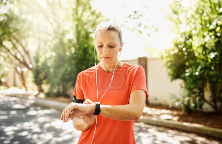 Téléchargez les photos : Fitness, running and watch with mature woman in street of neighborhood for cardio or physical activity. Break, exercise and time with athlete or runner outdoor for training or workout in summer. - en image libre de droit
