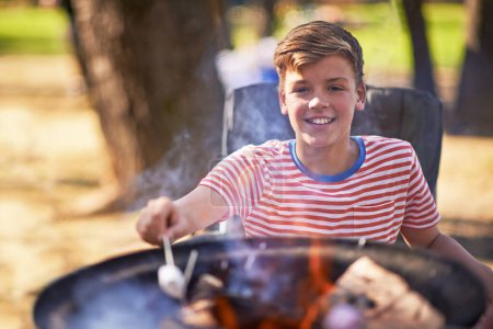 Boy, campfire and marshmallow for roasting, smile and happiness outside in nature. Camper, sunshine and vacation for relaxation, adventure and childhood memories with sweet snack and outdoor camping.