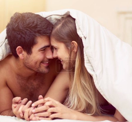 Blanket, smile and couple in bed for love with intimate moment, relationship bond and romantic together for trust. Bedroom, man and woman on mattress with relax for happiness, wellness and marriage.