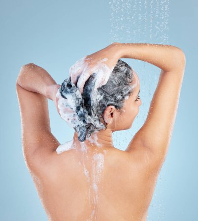 Téléchargez les photos : Femme, douche et cheveux pour shampooing en studio avec dos pour le nettoyage, la croissance et les pellicules sur fond bleu. Fille, personne et modèle avec gouttes d'eau pour produit, savon et mousse avec cuir chevelu bien-être. - en image libre de droit