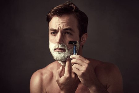 Man, blade and foam for shaving in studio, cleaning and skincare for grooming on black background. Male person, shaver and soap for hair removal or hygiene, dermatology and facial treatment tools.