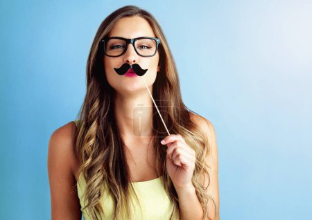 Girl, moustache and portrait or prop in studio with pout, photo booth and comic icon with mockup space. Woman, person and funny face with cardboard on stick for celebration and fun on blue background.
