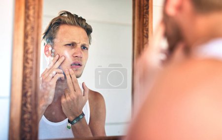 Man, acne and skincare in mirror of bathroom with facial cleaning, grooming and confused with pimple. Personal hygiene, person and unhappy with breakout, blackhead scar and morning routine in home.