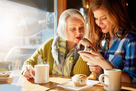 Lächelnd surfen Seniorin und Tochter im Café nach Erinnerungen mit den sozialen Medien und entspannen sich. Lustig, post- und technikaffin im Restaurant mit Kaffee, Muffin und Sonnenschein im Ruhestand
