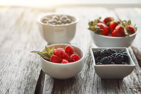 Bowls, berries and health on table, kitchen and organic choice for nutrition, breakfast and salad for wellness. Fruits, raspberry and mulberry in home with container, meal prep and food in morning.