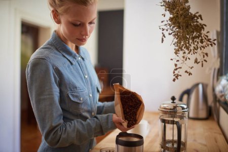 Photo for Woman, coffee beans and grinder in kitchen for drink preparation with plunger for morning, caffeine or latte. Home, brown bag and pour in machine on counter for hot beverage, matcha or cappuccino. - Royalty Free Image