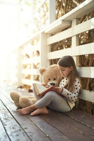Outdoor, teddy bear and girl with book for reading, education and language development. Backyard, toys and female child with textbook for storytelling, drawing and entertainment with fantasy.