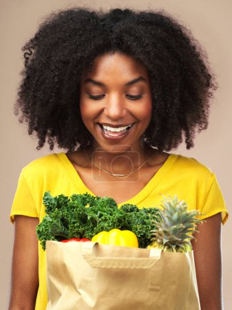 Black woman, grocery or package of vegetables and fruit in studio background smiling for eating healthy or delivery. Female person, happy and wellness food in bag for organic shopping and nutrition.