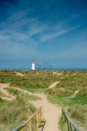 The sand dunes, and the grade II listed building Point of Ayr Lighthouse at Talacre beach in North Wales, UK on a sunny summer day.