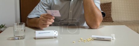 Photo for Worried man with hand in hair holding driving license with medicines like antidepressants and anxiolytics on the table. Effect of certain medicines on health and driving reflexes. Horizontal banner - Royalty Free Image