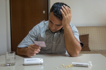 Photo for Worried man with hand in hair holding driving license with medicines like antidepressants and anxiolytics on the table. Effect of certain medicines on health and driving reflexes - Royalty Free Image