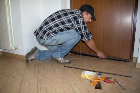 Handwerker montieren eine Staubdichtung an der Haustür. Bessere Wärmedämmung und Reinigung des Fußbodens.