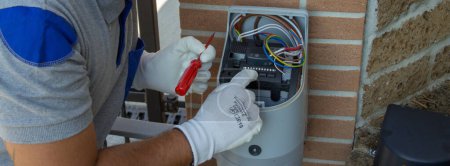 Electrician technician carrying out the repair and programming of a technical data sheet of the motor of an automatic driveway gate. Horizontal banner