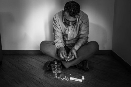 Foto de Imagen de un hombre sentado en el suelo en casa tomando medicamentos psiquiátricos como antiansiedad y antidepresivos. Drogodependencia y adicción. - Imagen libre de derechos