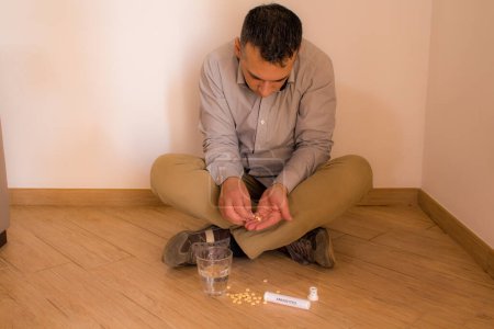 Foto de Imagen de un hombre sentado en el suelo en casa tomando medicamentos psiquiátricos como antiansiedad y antidepresivos. Drogodependencia y adicción. - Imagen libre de derechos