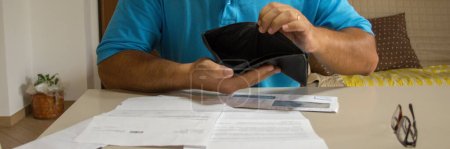 Photo for Image of a man's hands holding an open wallet with no money with various bills sitting on the table. Current economic and financial crisis. Horizontal banner - Royalty Free Image