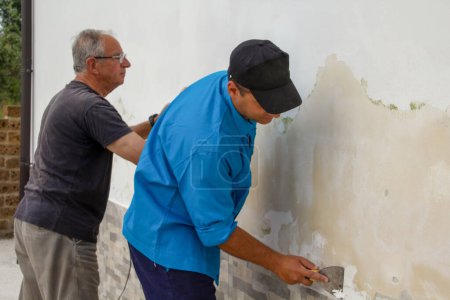 Téléchargez les photos : Image of two male construction workers sanding and cleaning a wall of mold. Rising damp problem. - en image libre de droit