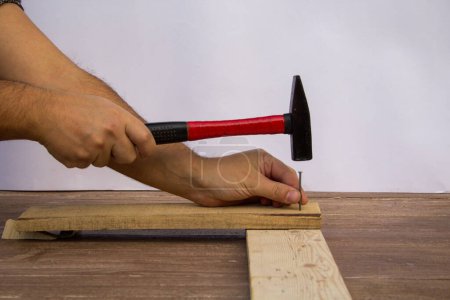 Téléchargez les photos : Image of a handyman craftsman's hands holding a hammer and nails while fixing wooden planks. - en image libre de droit