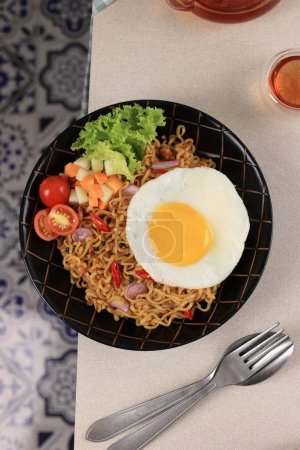Téléchargez les photos : Indomie Goreng ou Mie Goreng, nouille instantanée populaire indonésienne. Servi avec oeuf de côté ensoleillé, tomate, concombre. Vue du dessus - en image libre de droit