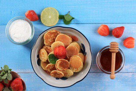 Photo for Bowl with Tiny Pancake Cereal with Strawberries and Mint Leaves on a Blue Wooden Background. Trendy food. Mini cereal pancakes. - Royalty Free Image