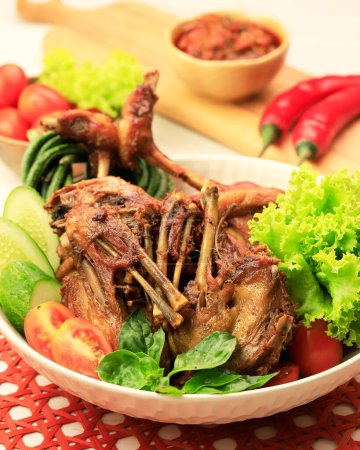 Foto de Bebek Goreng. Popular Indonesian Dish of Deep-fried Duck, Accompanied with Fresh Green Vegetables, Spicy Mango Pickles and Chili Paste. - Imagen libre de derechos