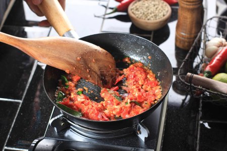 Foto de Cooking Process Saute Sambal or Sambel or Spicy Sauce with Lime Leaf on a Pan in the Kitchen using Wooden Spatula. Messy Kitchen during Cooking Backstage - Imagen libre de derechos