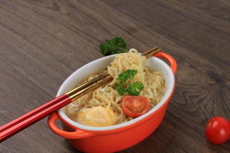 Téléchargez les photos : Fermer Indomie, nouilles instantanées indonésiennes savoureuses avec oeuf, tomate et piment haché sur bol à l'orange avec baguette. Sur la table avec espace de copie - en image libre de droit