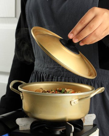 Téléchargez les photos : Cooking Ramyeon Korean Instant Noodle on the Stove, Female Hand Open Golden Pot Lid - en image libre de droit
