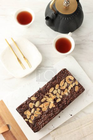 Téléchargez les photos : Brownie au caramel au chocolat avec pépites de chocolat et garniture de tranches d'amande, servi avec du thé - en image libre de droit