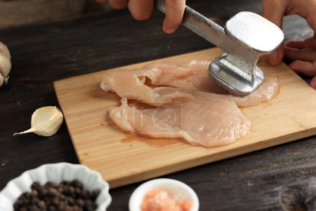 Téléchargez les photos : Cuisson de la viande de poulet au sein, battre le poulet à l'aide d'un attendrisseur de viande. Processus de cokéfaction dans la cuisine - en image libre de droit