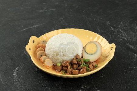 Foto de Nasi Bakmoy Ayam, arroz al vapor con salsa de soja mezclar pollo frito, medio huevo hervido, y pastel de camarones. En mesa de mármol negro - Imagen libre de derechos