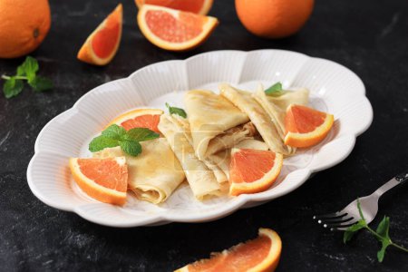 Téléchargez les photos : Suzette crêpe française traditionnelle avec sauce orange. Crêpes minces avec tranche d'orange fraîche sur plaque en céramique ovale. - en image libre de droit