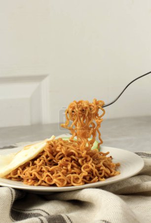 Téléchargez les photos : Mangez des nouilles frites Indomie Goreng, prenez des nouilles à la fourchette. Nouille instantanée indonésienne - en image libre de droit