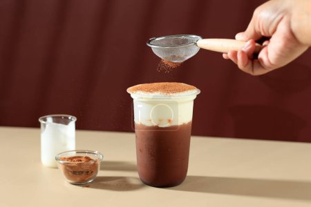 Foto de Manos vertiendo cacao en polvo a la bebida de crema de leche de chocolate, bebida asiática, espacio de copia para texto - Imagen libre de derechos