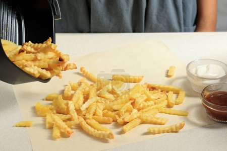 Photo for Pour Wavy Potato Crinkle Cut from Airfryer Tray to the Table. Cooking French Fries using Air Fryer - Royalty Free Image