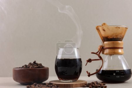 Cafetera Chemex de vidrio con sabroso café goteo y grano de café en la mesa marrón