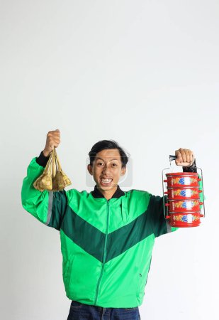 Foto de Conductor en línea masculino asiático excitado entregando Ketupat y guarnición en la lonchera apilable o Rantang, Eid Mubarak Cesta Concepto - Imagen libre de derechos