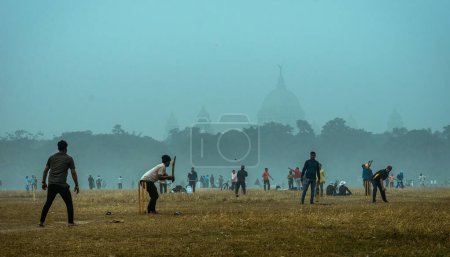 Foto de Kolkata, India - 15 de enero de 2023: Los chicos locales juegan un partido de cricket no organizado en una nebulosa mañana de invierno. Profundidad superficial del campo. - Imagen libre de derechos