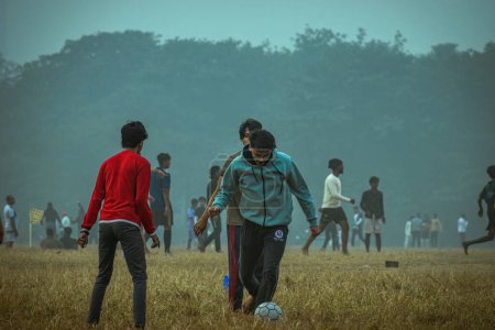 Foto de Kolkata, India - 15 de enero de 2023: Un grupo de chicos locales jugando un amistoso juego de fútbol no organizado en una fría mañana de invierno. Enfoque selectivo. - Imagen libre de derechos