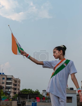 Foto de Linda niña india sosteniendo bandera india contra el cielo celebrando el Día de la Independencia india mostrando patriotismo. Enfoque selectivo en la cara - Imagen libre de derechos